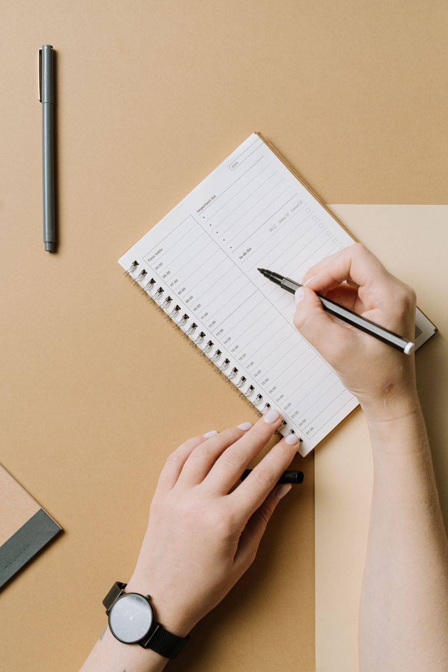 Hands writing in a daily planner with an hourly timetable and to-do list