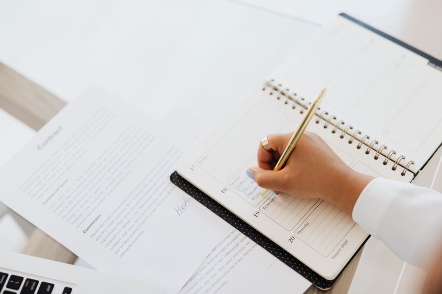 Hand writing in a spiral planner beside a contract document on a desk