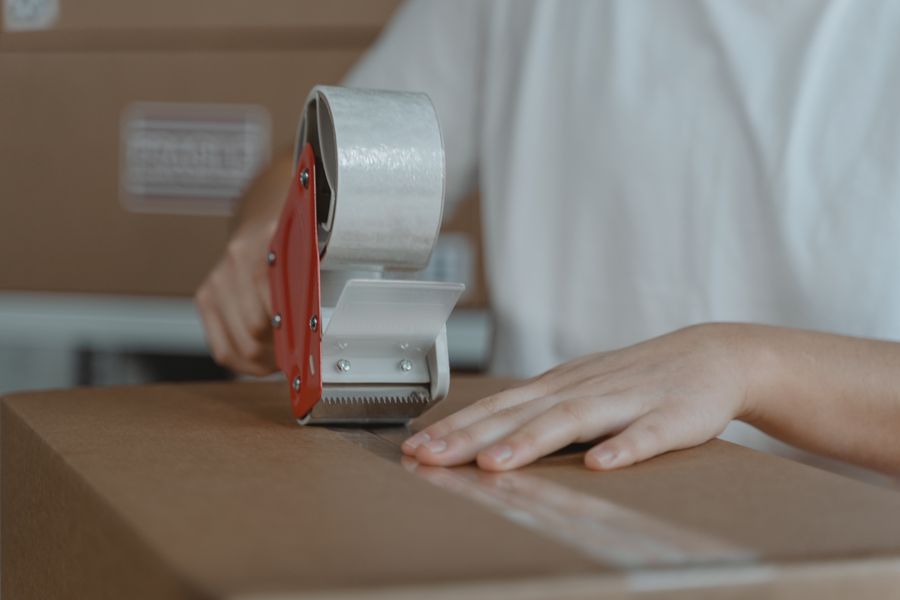 Hands sealing a cardboard box with a tape dispenser