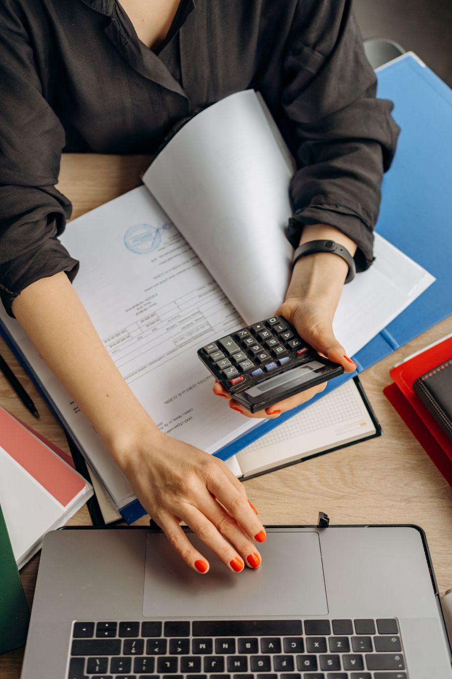 Person using a calculator over financial documents and a ledger