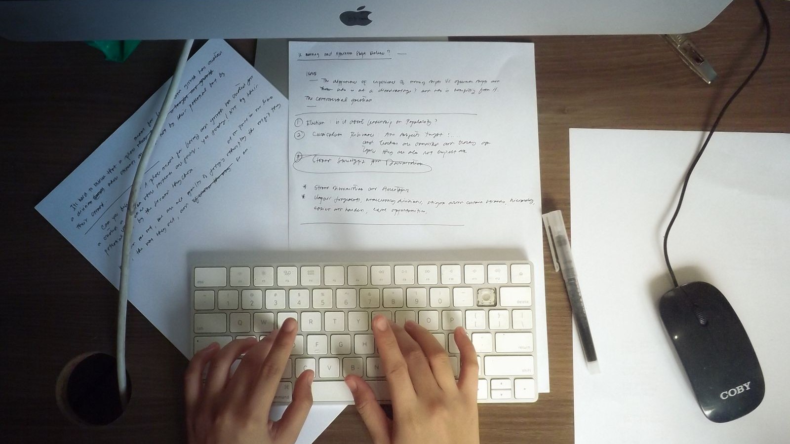 Hands typing on a white desktop keyboard, with handwritten notes on paper beside it