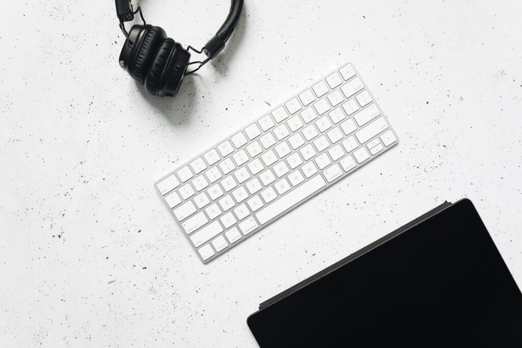Overhead view of headphones and a keyboard on a clean white desk, the tools of phone-free remote work