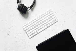Overhead view of headphones and a keyboard on a clean white desk, the tools of phone-free remote work