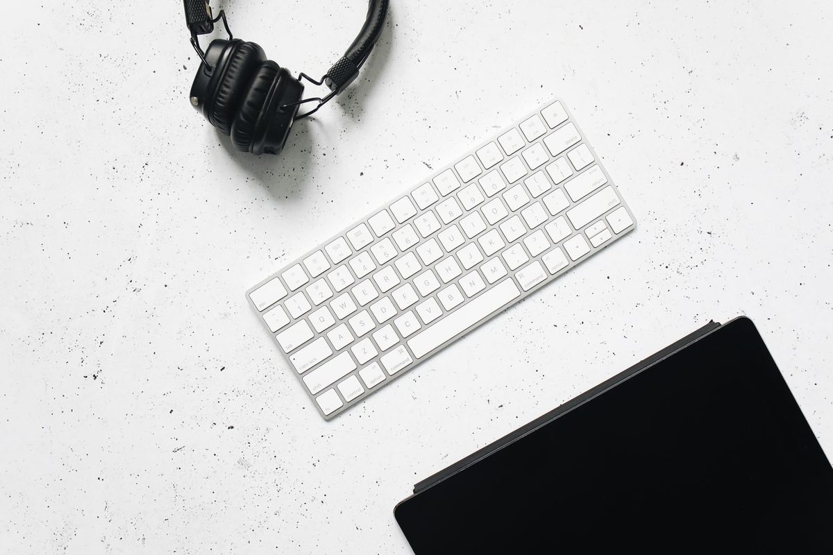 Overhead view of headphones and a keyboard on a clean white desk, the tools of phone-free remote work