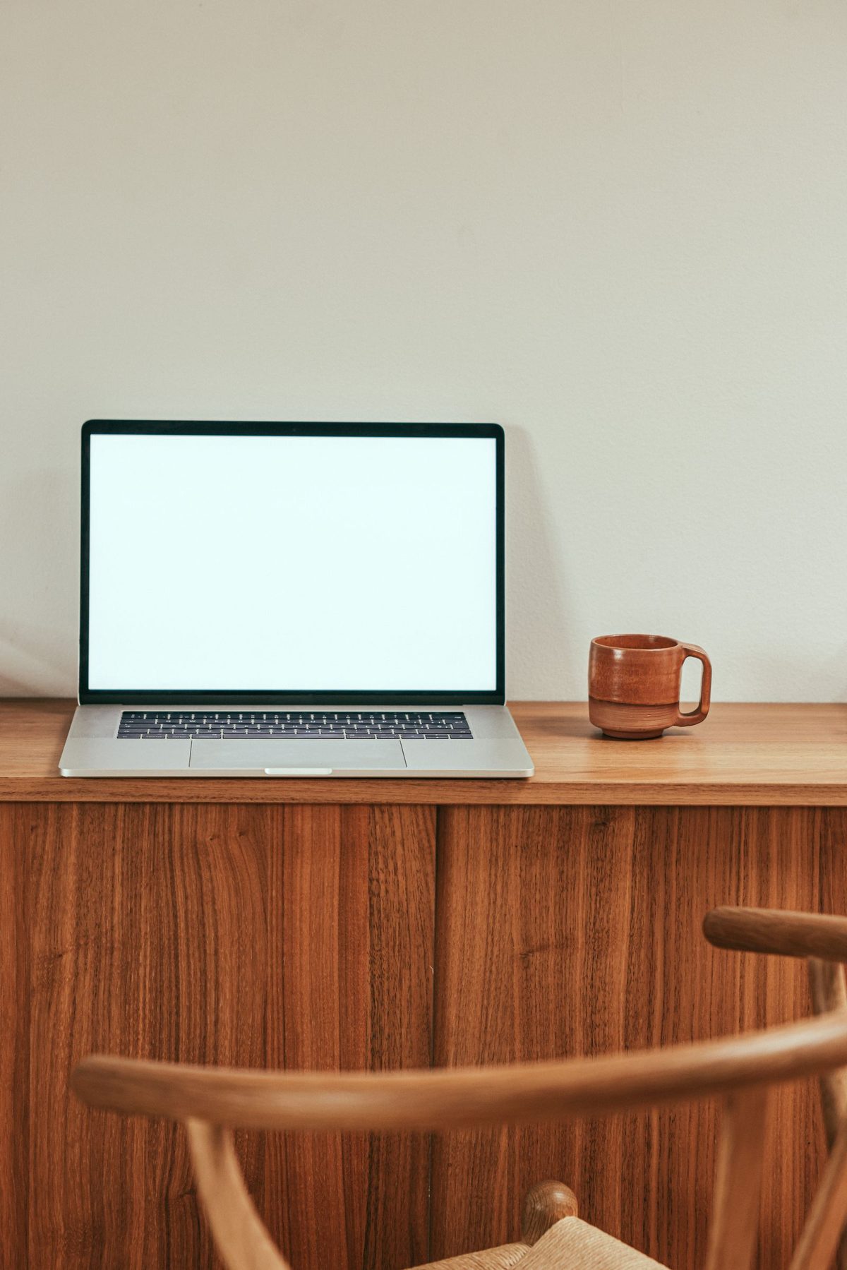 Wooden chair pulled up to a wooden desk with an open laptop and a coffee mug, a minimalist home-office workspace