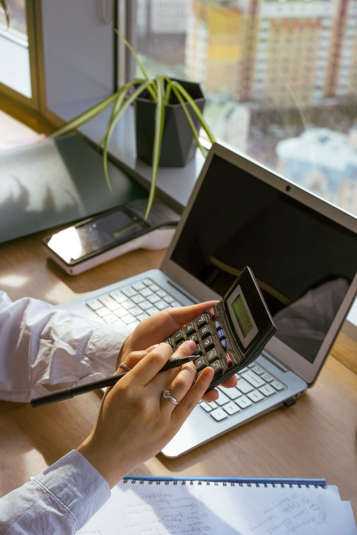 Person calculating at a desk with a laptop and notebook
