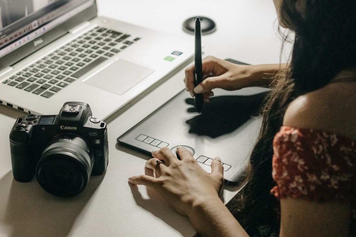 Woman creating digital art on a graphics tablet beside a laptop