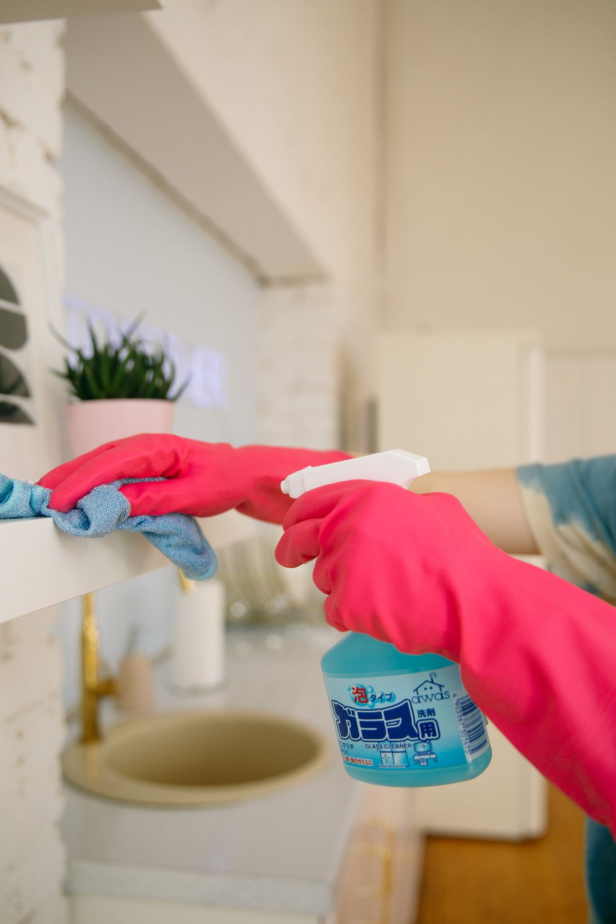 Person cleaning a kitchen shelf with a spray bottle and cloth