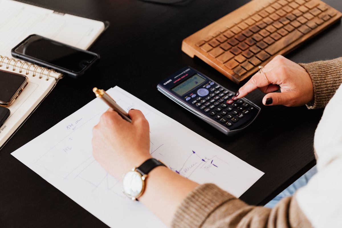 Hands working a calculator and notebook over documents