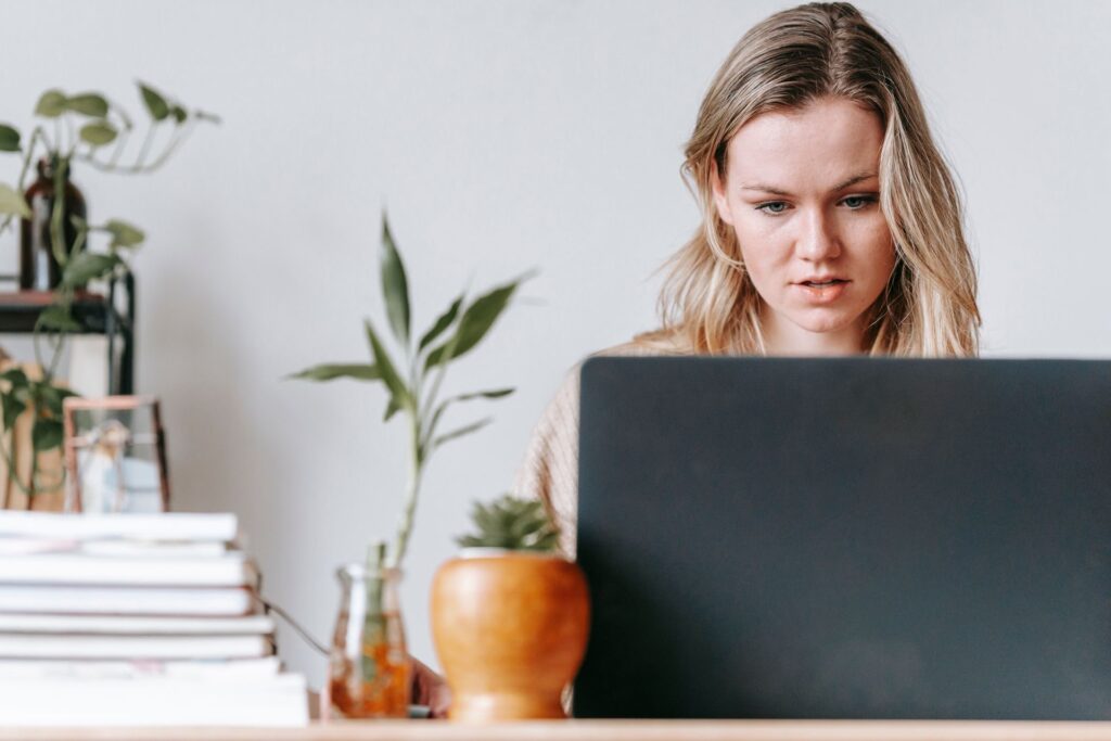 A young woman concentrating on her laptop in a home office with houseplants and books