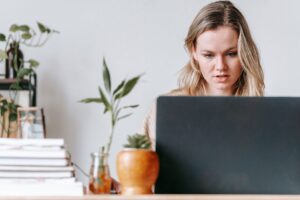 A young woman concentrating on her laptop in a home office with houseplants and books