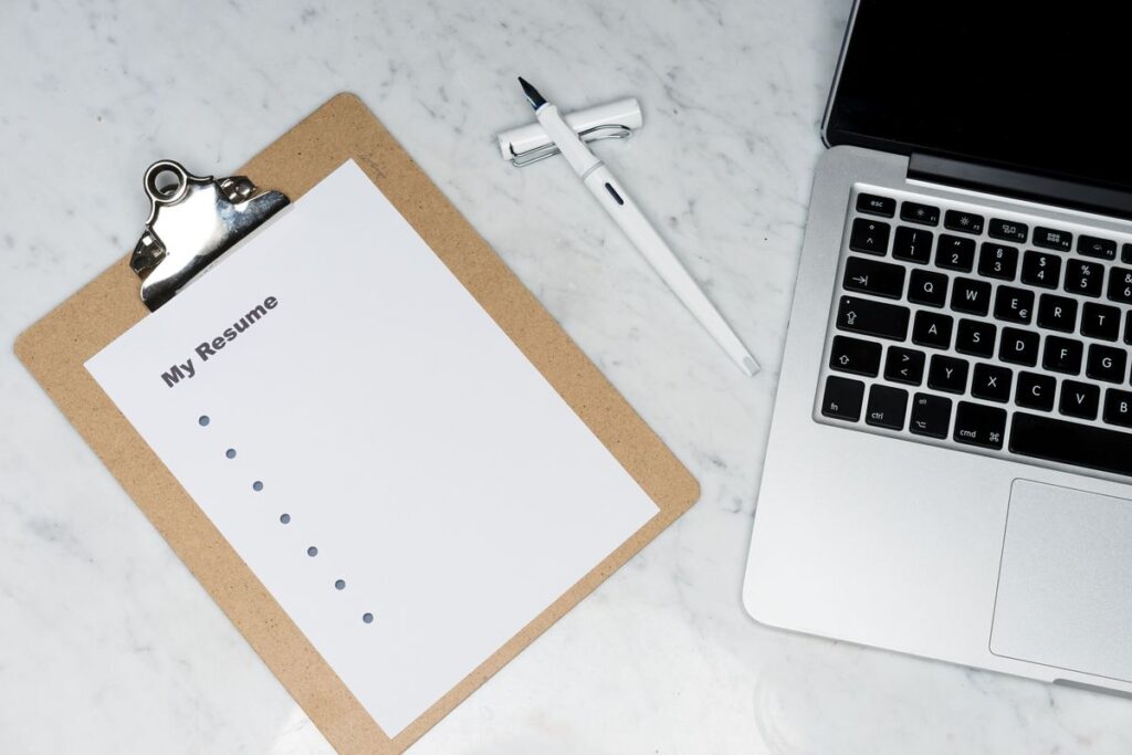 Clipboard with a resume beside a pen and laptop on a desk